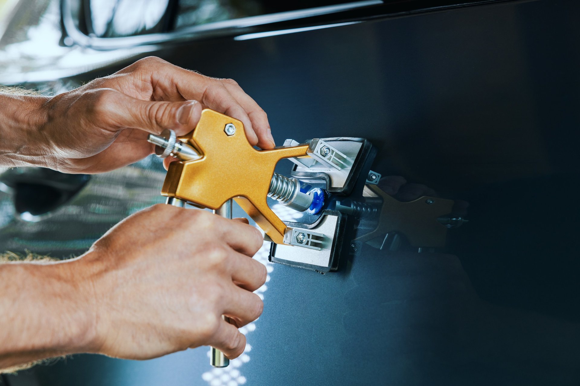 Paintless car dent repair tool. Man fixing vehicle door with PDR technology