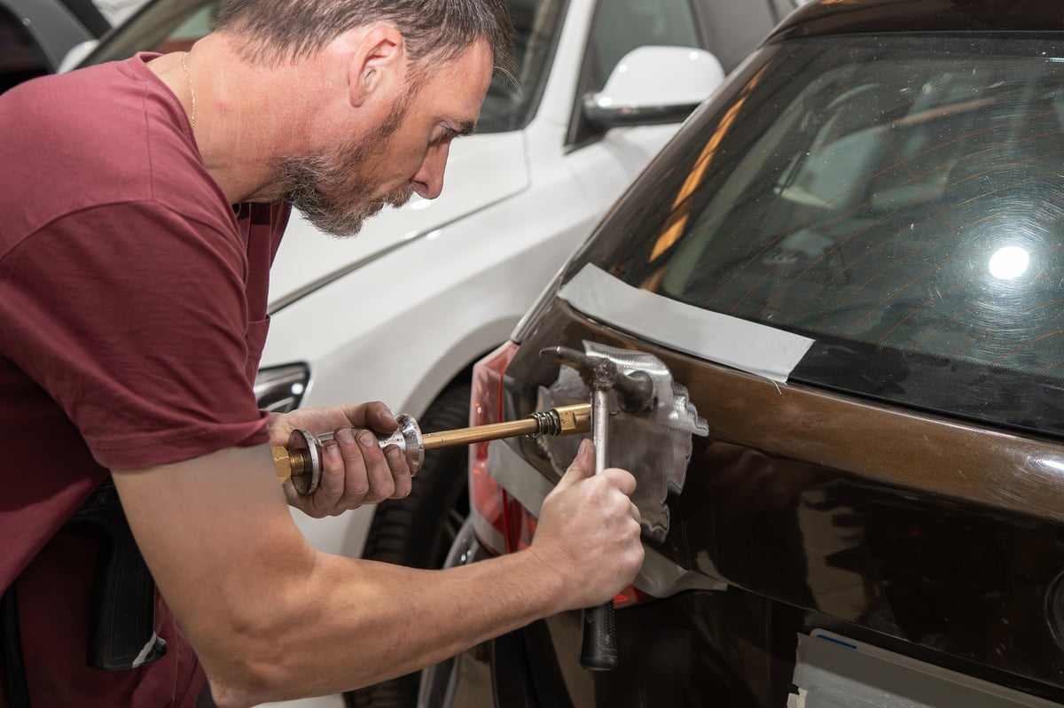 Mechanic employs a slide hammer to pull out a dent on the rear door of a car in an auto repair shop