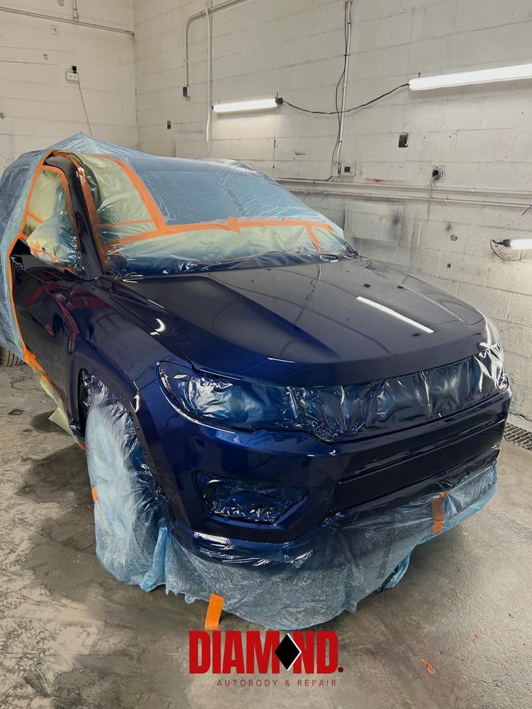 Blue SUV with protective plastic wrap and orange masking tape in an auto body shop