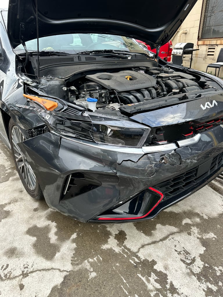 Damaged gray Kia vehicle with open hood showing engine, front bumper crushed, parked in lot