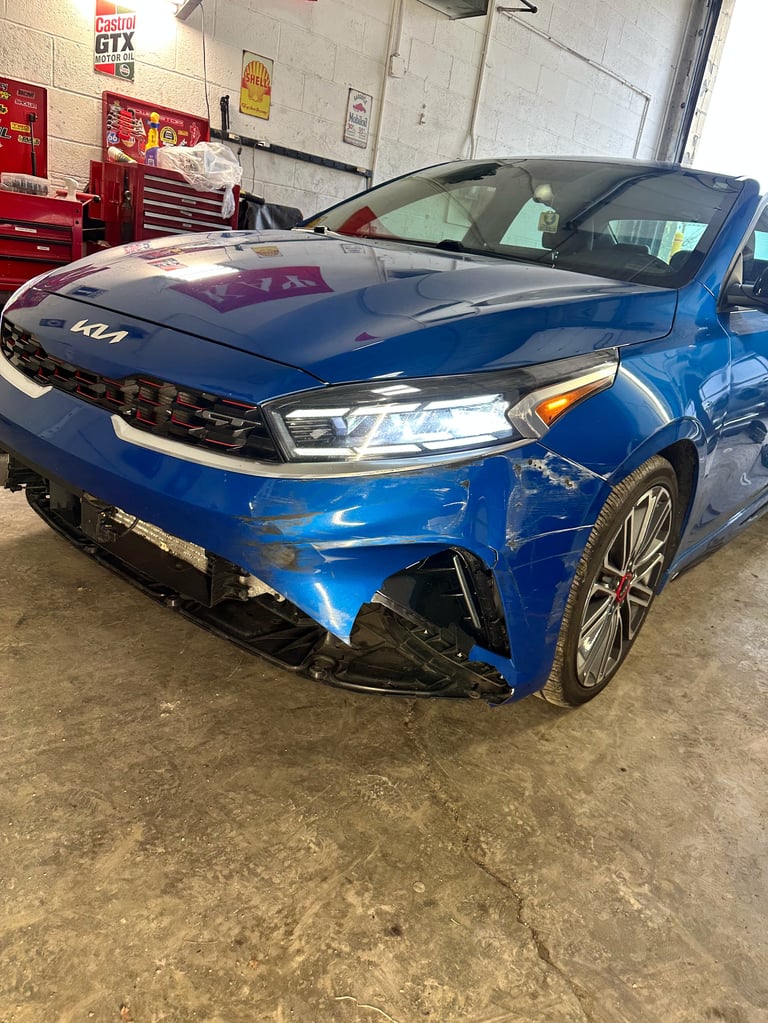 Blue Kia vehicle with front-end damage in an auto repair shop garage