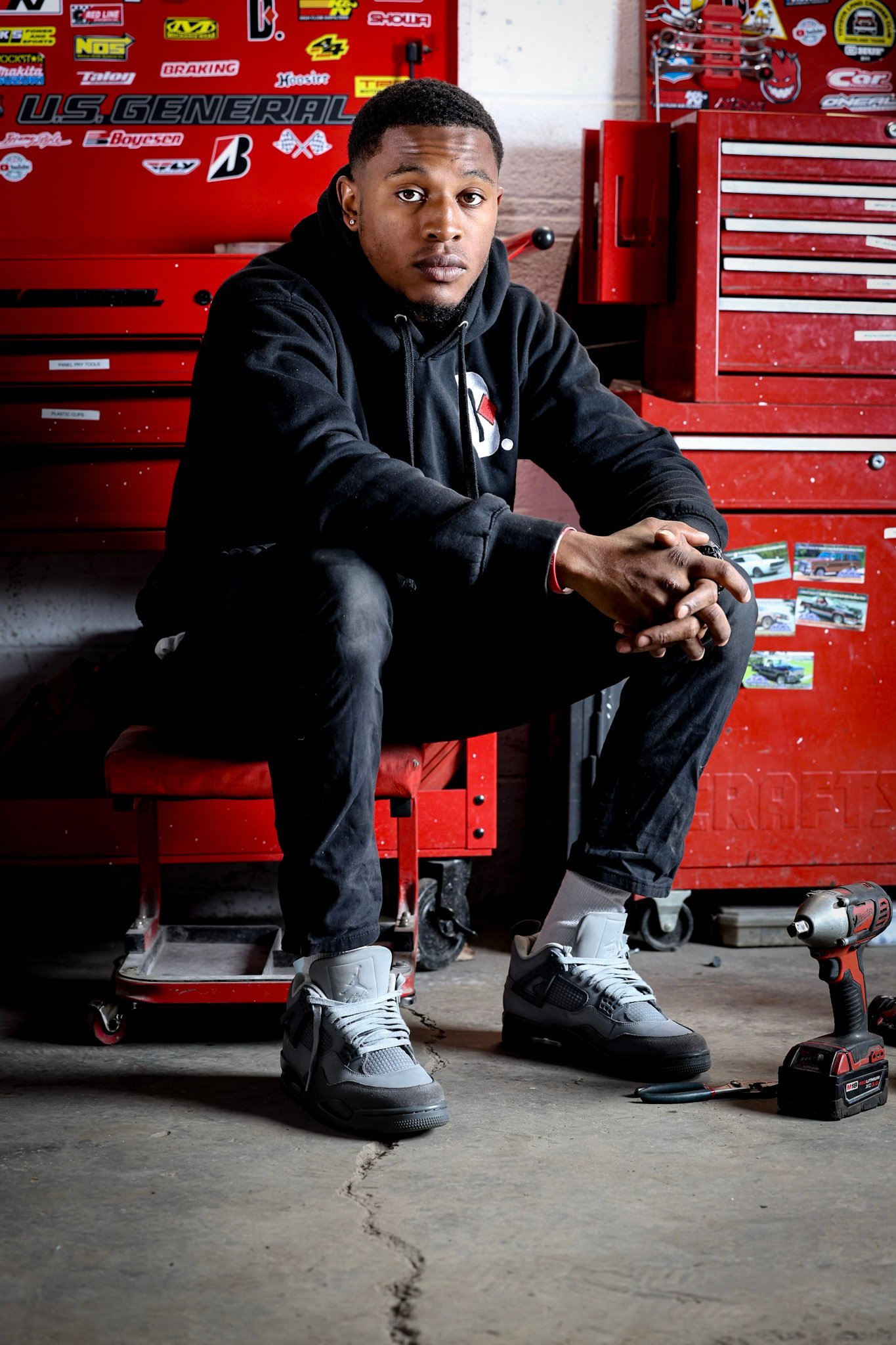 Man in black hoodie sitting on red tool chest in garage workshop, posing for portrait