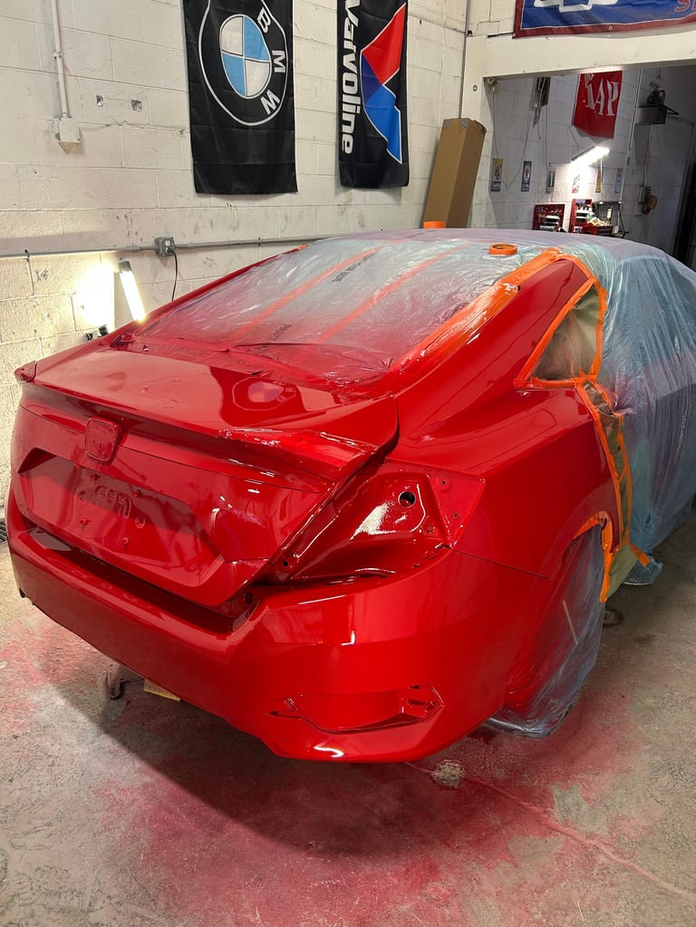 Red car covered in plastic sheeting inside a garage workshop with BMW and Audi flags on the wall