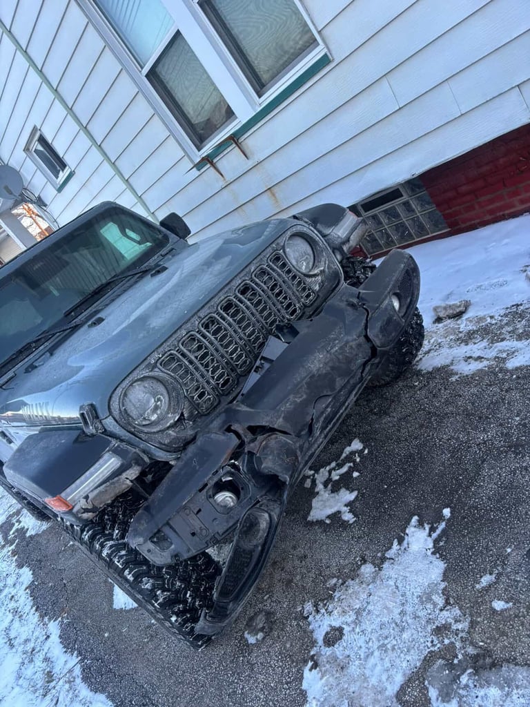 Dark blue Jeep Wrangler parked in snow and slush in front of a modern building with metal siding