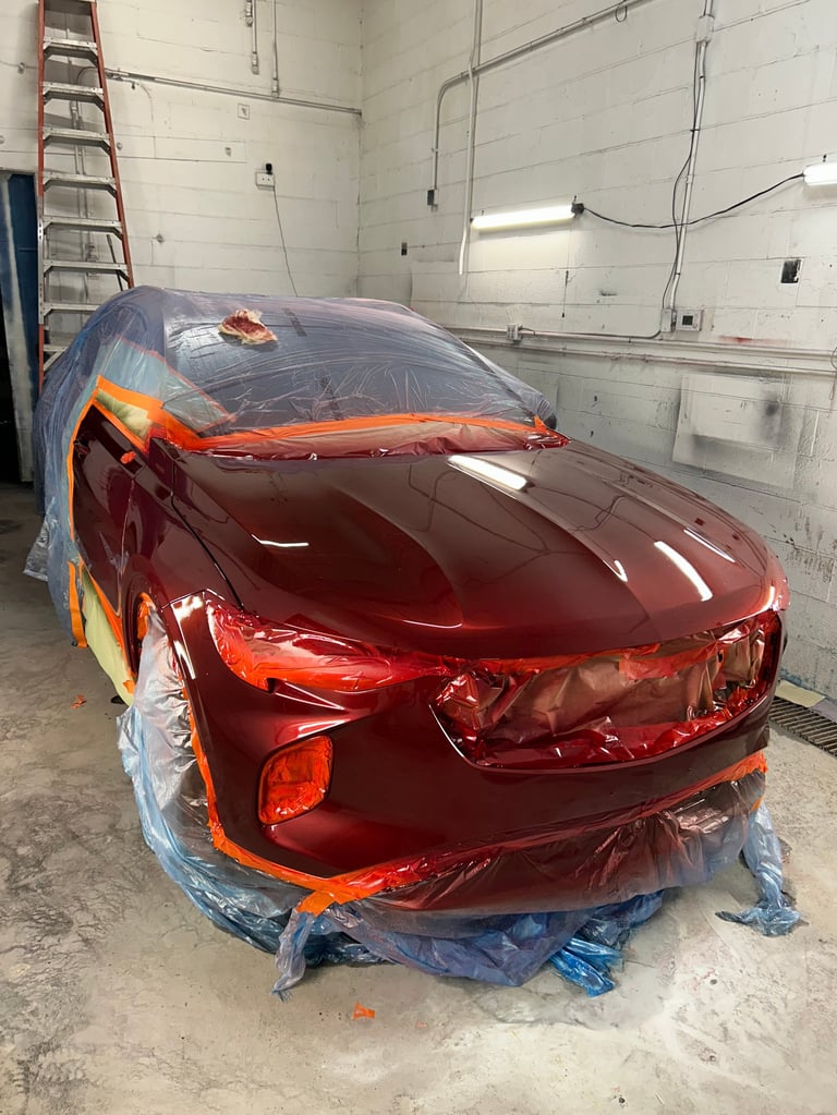 Red vehicle wrapped in blue and orange protective plastic sheeting inside a garage workshop