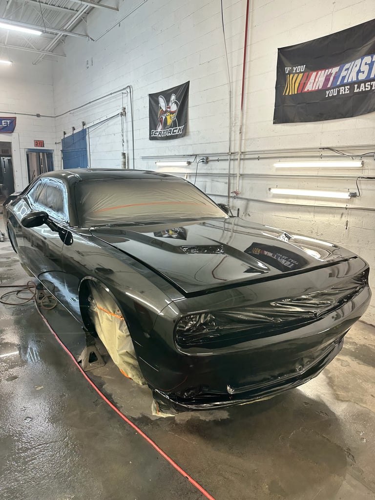 Black sports car with hood open in a garage workshop with white walls and motivational signage