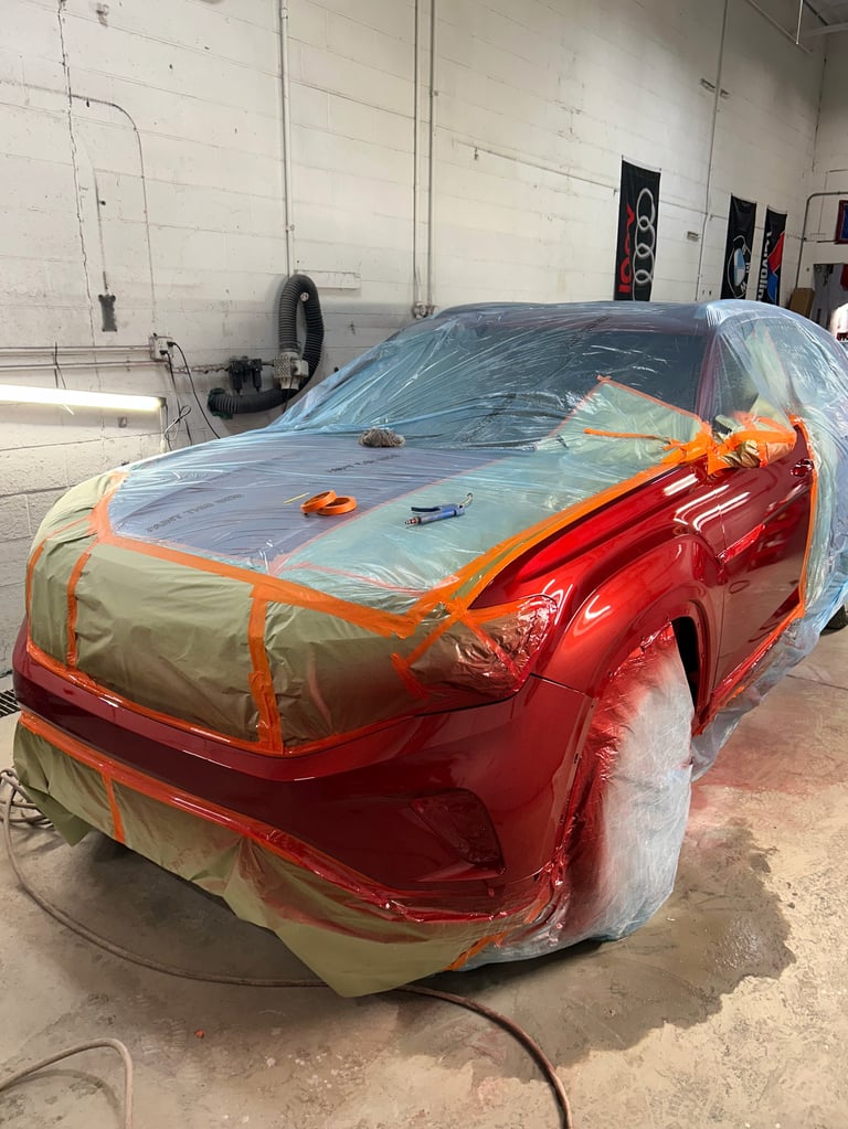 Red car covered with protective plastic sheeting and painters tape in an auto body shop garage